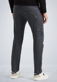 Dunkelgraue Cargo-Hosen mit slim fit, die mehrere Taschen, eine gestickte Textur und kontrastierende Stoffakzente aufweisen. Weiße Sneakers vervollständigen das Outfit.