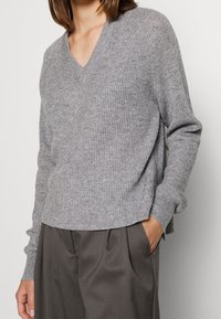 Maglione grigio a coste con scollatura a V, dalla vestibilità rilassata e maniche lunghe. Indossato sopra pantaloni grigi a vita alta e dalla vestibilità ampia.