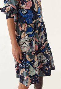 Blumenmuster-Kleid mit Rüschenschichten, überwiegend navy mit rosa, blauen und grünen Akzenten. Aus leichtem, strukturiertem Stoff gefertigt.