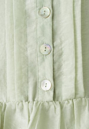 Close-up of pale green fabric with three iridescent round buttons and gathered stitching near the bottom edge.