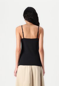 Svart tettsittende camisole med justerbare tynne stropper, en rund halsutskjæring, og glatt stoff. Brukt med et lysebeige skjørt.