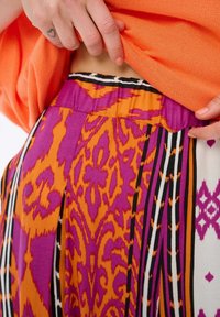 Kolorowa tkanina w desenie z pomarańczowymi, fioletowymi i białymi sekcjami. Oferuje wyraziste wzory, tekstury oraz fałdy w okolicy pasa.