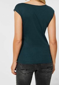 Tealfärgad kortärmad topp med bred ringning, slät textur och figursydd passform, i kombination med mörkgrå jeans med unik fickstitching.