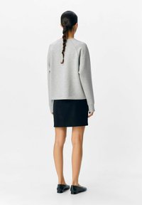Grå sweatshirt med raglanærmer, parret med en sort nederdel. Glat stoftekstur, afslappet design og ankelhøje sorte sko.