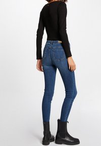 Blå denim skinny jeans med hög midja och bakfickor, kombinerat med svarta ankelskor och en figursydd svart långärmad topp.