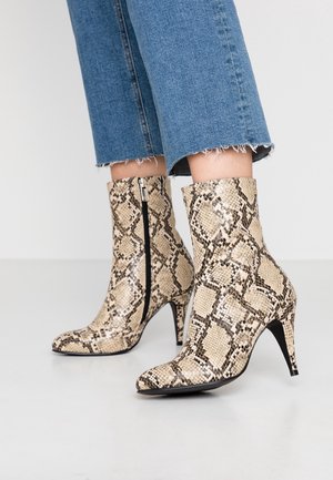 Bottes à bout pointu montantes à la cheville avec imprimé serpent beige et noir, portées avec un jean bleu court aux ourlets effilochés.