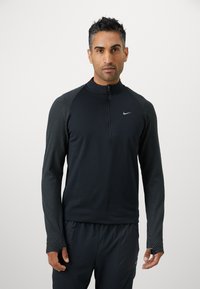 Sort atletisk langærmet trøje med kvart lynlås, teksturerede stribede skulderpaneler og et lille Nike-logo på brystet. Letvægtigt materiale.