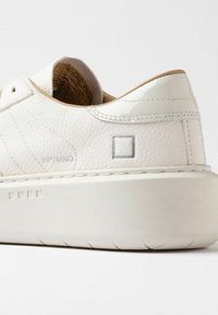 Hvid læder sneakers i nærbillede, der viser den teksturerede overdelen, polstret krave, syet sål og et minimalistisk firkantet logo på siden.