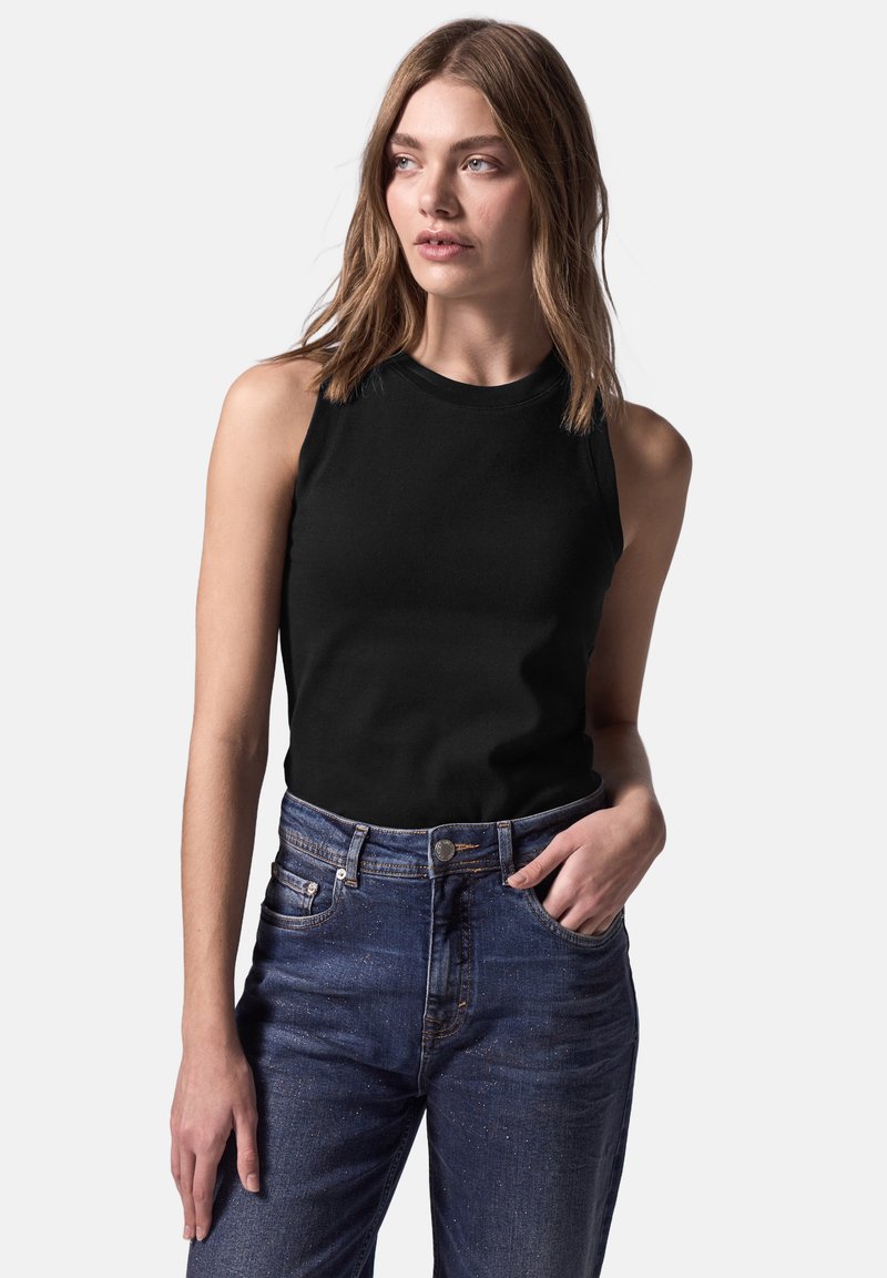 Top negro sin mangas con escote redondo, combinado con jeans de mezclilla azules de cintura alta y un leve acabado desgastado.