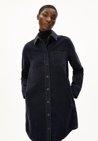 Dunkelblaues Denimhemdkleid mit langen Ärmeln, durchgehender Knopfleiste und Brusttasche. Es hat einen Kragen und einen leicht abgerundeten Saum.