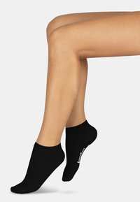 Schwarze Knöchelsocken aus einem weichen Stoff, mit einem gerippten Bund und einem Logo, das an der Seite aufgedruckt ist. Sie haben eine glatte Textur und eine enganliegende Form.