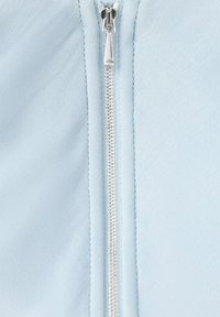 Fermeture éclair en métal argenté fermée sur un tissu bleu clair avec des coutures visibles le long des bords de la fermeture éclair.