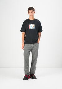 Black t-shirt with a colorful graphic print, paired with gray denim jeans and black sneakers with red accents. Simple, relaxed-fit design.