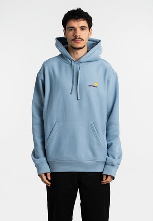 Sudadera de algodón azul claro con un bolsillo frontal, capucha con cordón y logo bordado en amarillo y rojo en el pecho. Corte relajado.