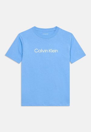 Lys blå kortermet t-skjorte med hvit «Calvin Klein»-logo sentrert på fremsiden, vist mot en enkel lys bakgrunn.