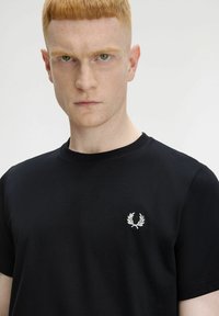 T-shirt in cotone nero con collo rotondo e maniche corte, decorato con una ghirlanda di alloro ricamata in bianco nell'area del petto sinistro.