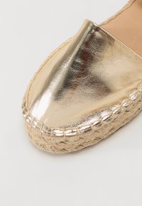 Gouden metalen espadrille met een spitse neus, jute touwzool en gestikte accenten. Gladde textuur met een glanzende afwerking.