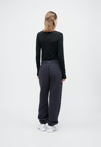 Melna garām piedurknēm blūze, apvienota ar brīvi krītošām pelēkām quiltēta auduma biksēm ar viļņveida rakstu, elastīgu jostu un aprocēm potītēs.