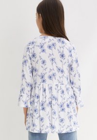 Top in cotone bianco con motivo floreale blu, con maniche lunghe, vita arricciata e scollatura rotonda. Tessuto morbido con un design fluido.