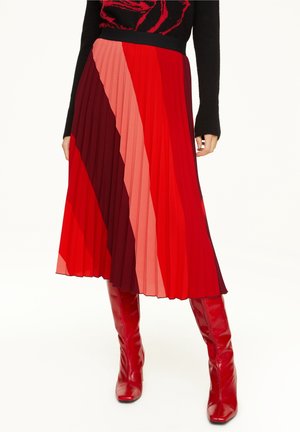 Rode geplooide midirok met verschillende tinten rood en bordeaux in diagonale strepen, gecombineerd met glanzende rode kniehoge laarzen.