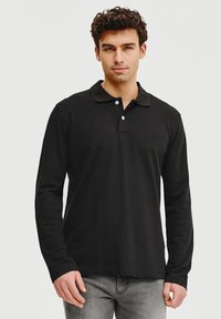 Czarna koszulka polo z długim rękawem o miękkiej strukturze, z zapięciem na dwa guziki i klasycznym kołnierzykiem, w zestawie z jasnoszarymi dżinsami.