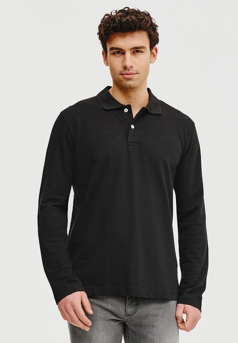 Czarna koszulka polo z długim rękawem o miękkiej strukturze, z zapięciem na dwa guziki i klasycznym kołnierzykiem, w zestawie z jasnoszarymi dżinsami.