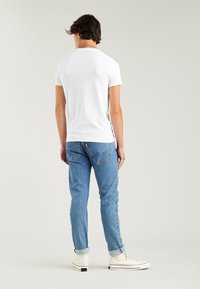 White cotton t-shirt, short sleeves, standard fit, paired with light blue straight-leg jeans and white high-top sneakers. Plain design, no patterns.