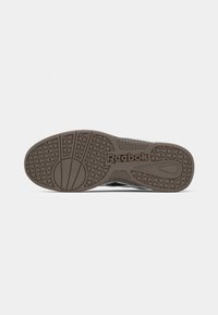 Apavu zole ar reljefu, kas nodrošina saķeri, ar aplokšņu un trīsstūrveida dizainiem, un centrā uz brūnas gumijas zolēm ir iegravēts "Reebok" logo.