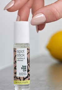 Bâtonnet en verre clair avec un capuchon blanc. Présente un motif floral noir et du texte. Contenu visible ; accent jaune citron à la base.
