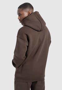 Sudadera con capucha marrón de corte relajado, con puños y dobladillo de canalé. Tejido suave con una textura lisa, que presenta un diseño de gran capucha.
