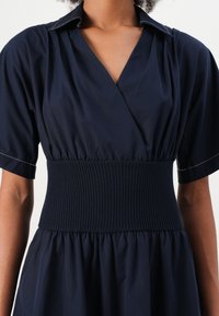 Vestido de marinheiro com mangas curtas, decote em V, faixa de cintura canelada e saia com pregas. Tecido suave com detalhes em costura contrastante.