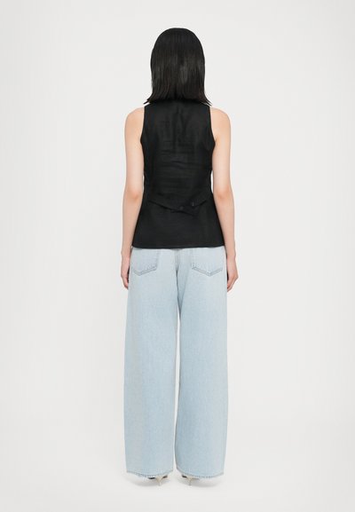 Black sleeveless top with a structured design, featuring a back button closure and beige wide-leg jeans with front pockets and a light wash.