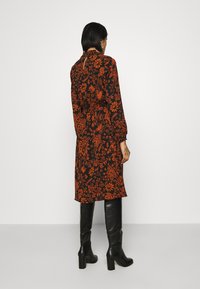 Černé šaty s oranžovým květinovým vzorem, dlouhými rukávy a vysokým výstřihem. V kombinaci s černými kozačkami po kolena a elegantní siluetou.
