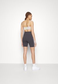 Grå høy midje shorts med sidestriper og en lett mønstret bralette. Modellen står foran en nøytral bakgrunn og har på seg hvite sneakers.