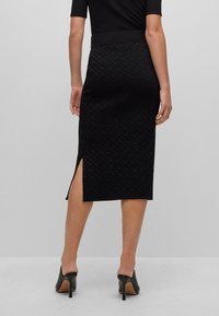 Schwarze Midi-Rock mit subtiler Textur, seitlichem Schlitz und tailliertem Bund, kombiniert mit schwarzen High Heels.