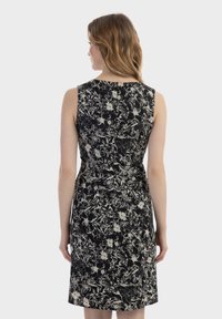 Schwarzes Blumenkleid mit taillierter Passe und ärmellosem Design. Besitzt ein weißes Blumenmuster. Die Rückansicht zeigt eine glatte, maßgeschneiderte Silhouette.
