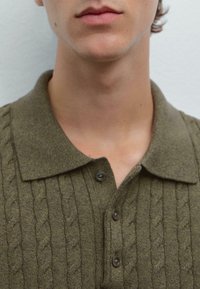 Polo shirt verde oliva, in maglia texturizzata, con colletto e tre bottoni neri. Presenta un motivo a trecce e un tessuto morbido.