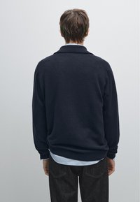 Námořnický pletený svetr s měkkou texturou a uvolněným střihem, s límcem a vrstvený přes světle modrou košili, doplněný o tmavé džíny.