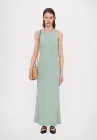Robe maxi sans manches vert menthe avec un col rond. Tissu lisse et ajusté qui descend jusqu'au sol. Sac à main en toile et chaussures noires complètent le look.