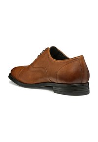 Scarpa da dress in pelle marrone con punta arrotondata, texture liscia, cuciture sottili e suola in gomma nera. I lacci sono visibili nella parte superiore.