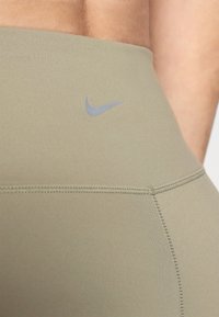 Zelene tajice od glatkog, rastezljivog materijala. Imaju sivi Nike logotip blizu struka i vidljive detalje šivanja.