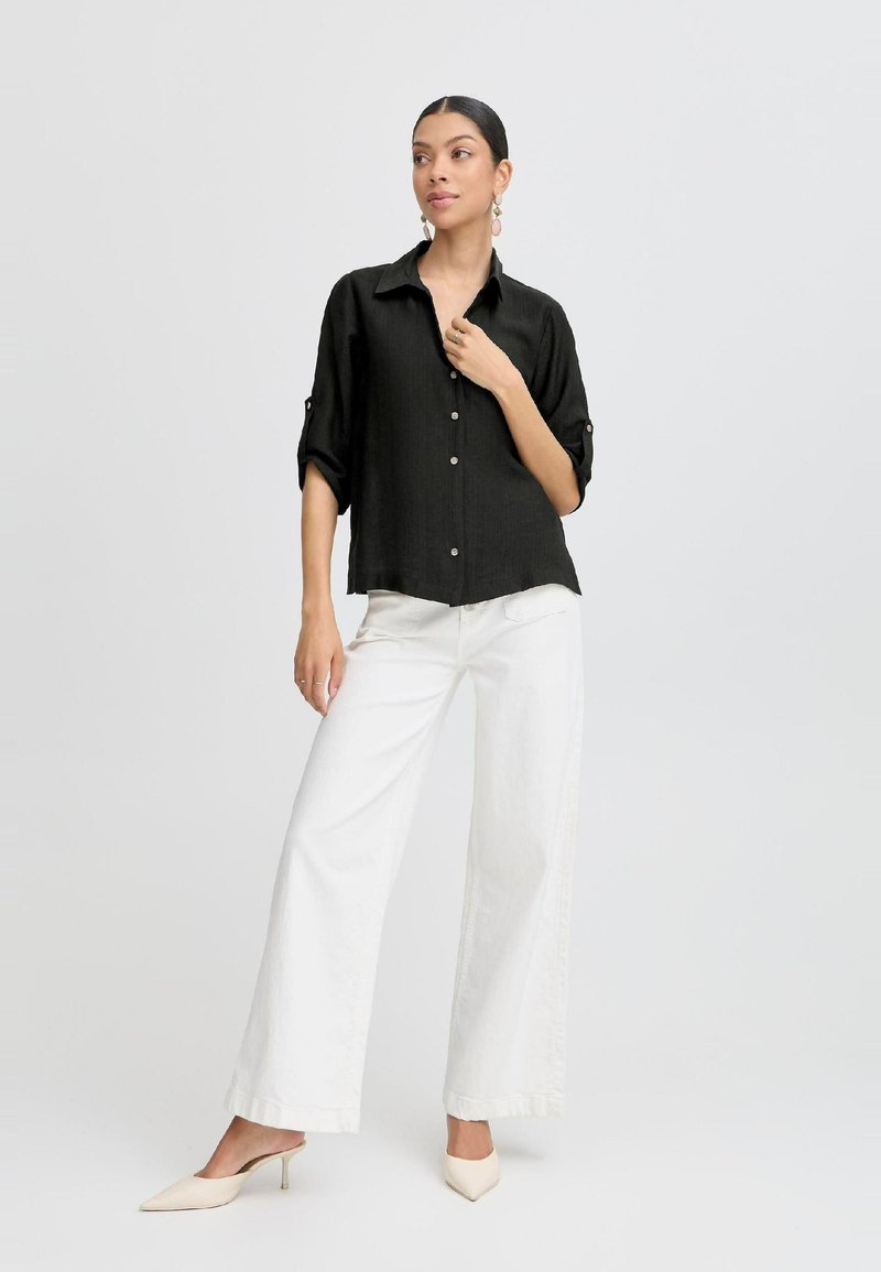 Camicia nera da donna con bottoni, maniche arrotolate, abbinata a pantaloni larghi bianchi. Tessuto liscio e design classico del colletto.