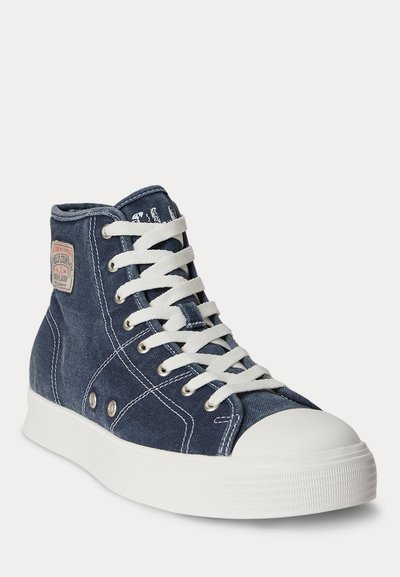 High-top sneaker in dark blue denim with white laces, thick white rubber sole, stitching details, and a small fabric brand patch on the side.