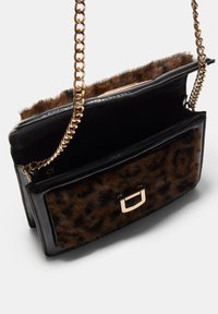 Borsa a spalla in pelle nera con tasca anteriore in pelliccia di leopardo, chiusura in oro e tracolla in catena dorata, mostrata aperta su sfondo bianco.