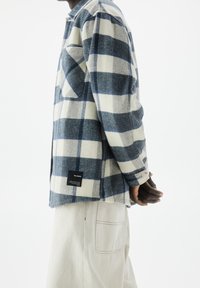 Camicia in flanella a quadri navy e crema, con tasca, polsini a bottone e un'etichetta quadrata sull'orlo inferiore. Il tessuto sembra morbido e strutturato.