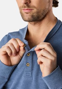 Långärmad tröja i wafflestickning i ljusblått, med en henley-krage och träknappar, delvis uppknäppt. Slät tygkvalitet.