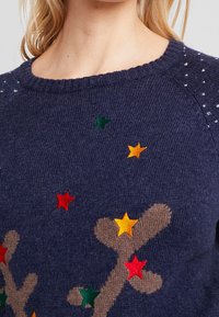 Pull en tricot bleu marine avec un col rond, orné d'étoiles brodées colorées en rouge, jaune, vert et marron.
