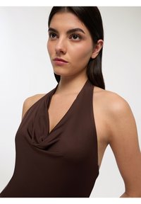 Top marrone con scollatura a halter e design drappeggiato sul davanti. Tessuto liscio e elegante con silhouette aderente e stile minimalista.