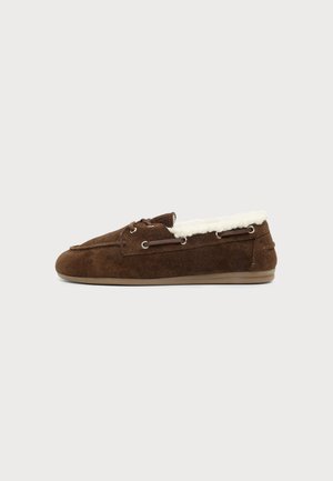 Καφέ μοκασίνι στυλ παντόφλα από δέρμα σουέτ με λευκή επένδυση από φλις και λαστιχένια σόλα, απεικονίζεται σε πλαϊνή όψη σε φωτεινό φόντο.