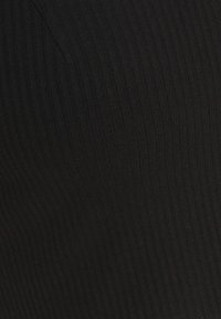 Gros plan d'un tissu côtelé noir montrant des lignes verticales texturées et une légère couture courbée.